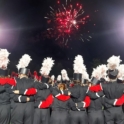 Dozens of teens in black and red band uniforms link arms and watch fireworks