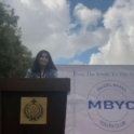 Lea Yes Alumna From Lebanon Stands At A Podium In Front Of A Banner Reading From The Youth To The Village Majdel Baana Youth Club
