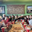  Over a dozen teens eat pizza together around a big table