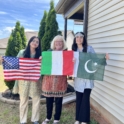 Two students and their host mom in Pakistani dress, holding flags