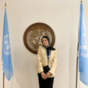 Yasmeen standing in front of the UN logo